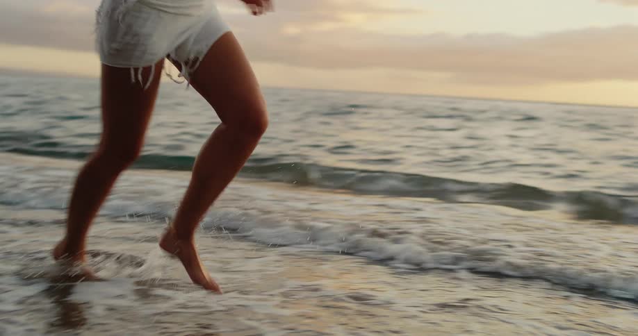 A female runs barefoot along the shoreline as waves wash up on the sand