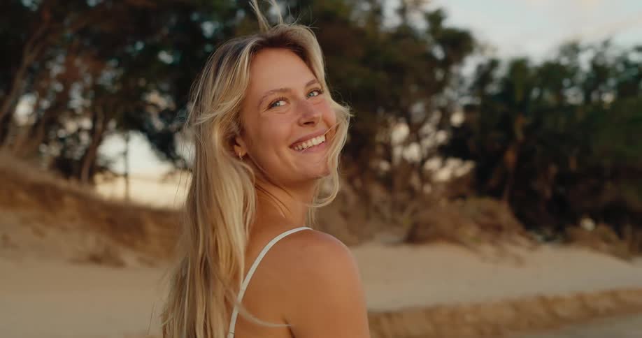 A long haired blonde female walks while smiling outdoors