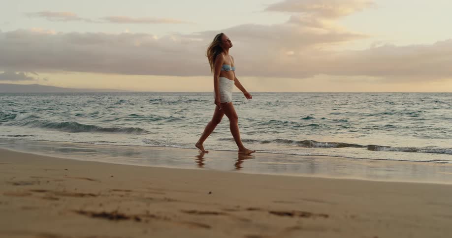 A female walks along the shoreline at sunset
