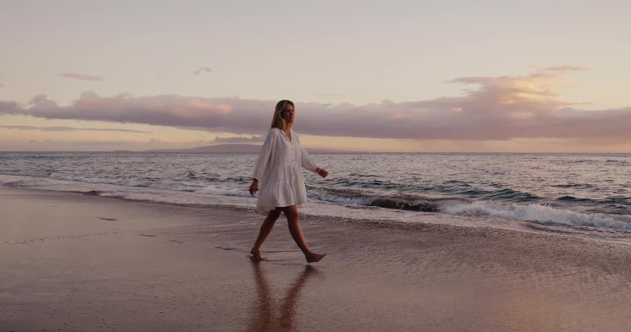 A young woman walks along the seashore at sunset