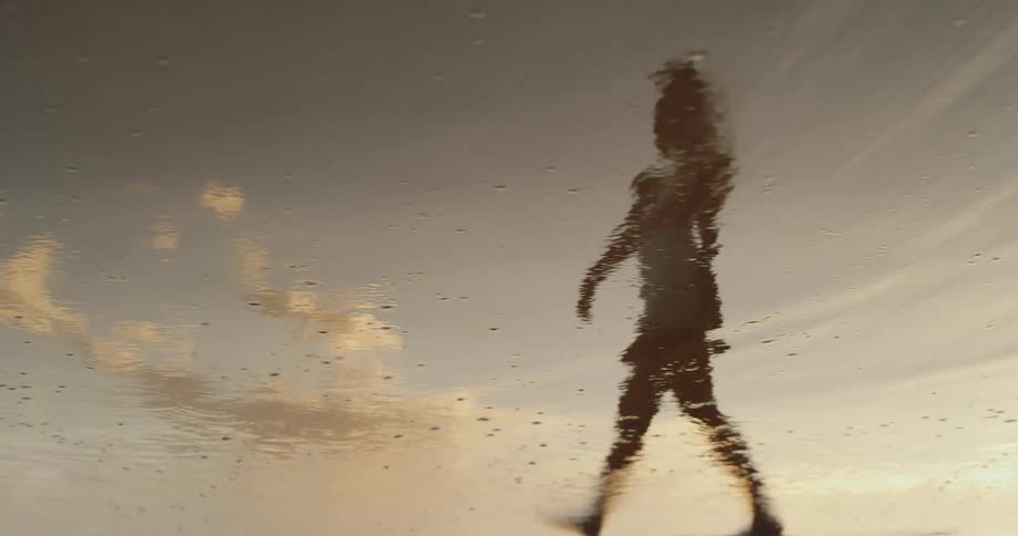 Reflection of a person walking on wet sand at sunset