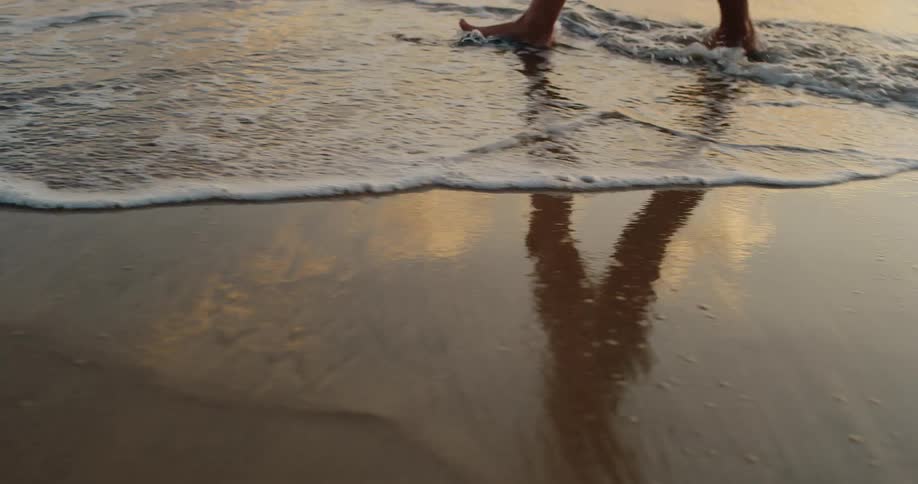 Feet of a barefoot person walking in the water with gentle waves on the beach