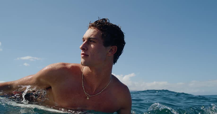 A man rests on a surfboard and moves his body with the movement of the water