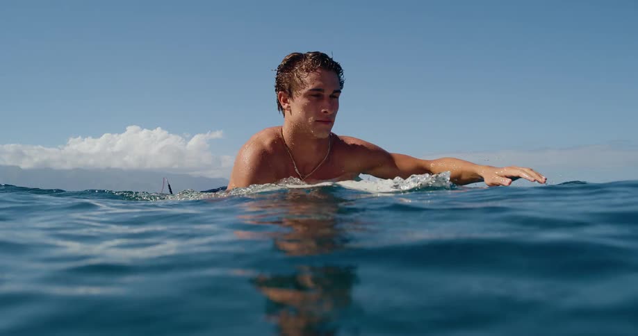 A man lies on a surfboard and paddles in the water