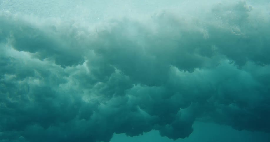 The camera is submerged under the ocean surface and captures a wave breaking and producing bubbles