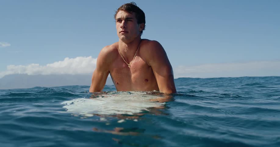 A young man swimming in the ocean while riding a surfboard at midday