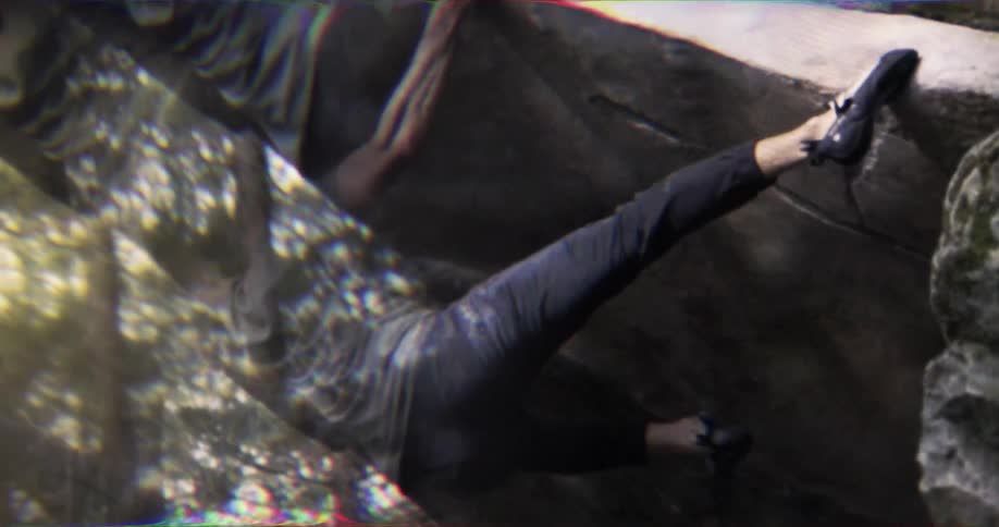 A closeup shot shows a male rock climber wearing a gray tshirt and dark pants gripping the rock with his hands and feet the camera has a slightly distorted lensflare effect as it follows his movements while he climbs