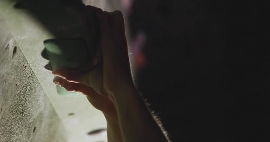 Pair of hands holding onto a handhold of an indoor climbing wall