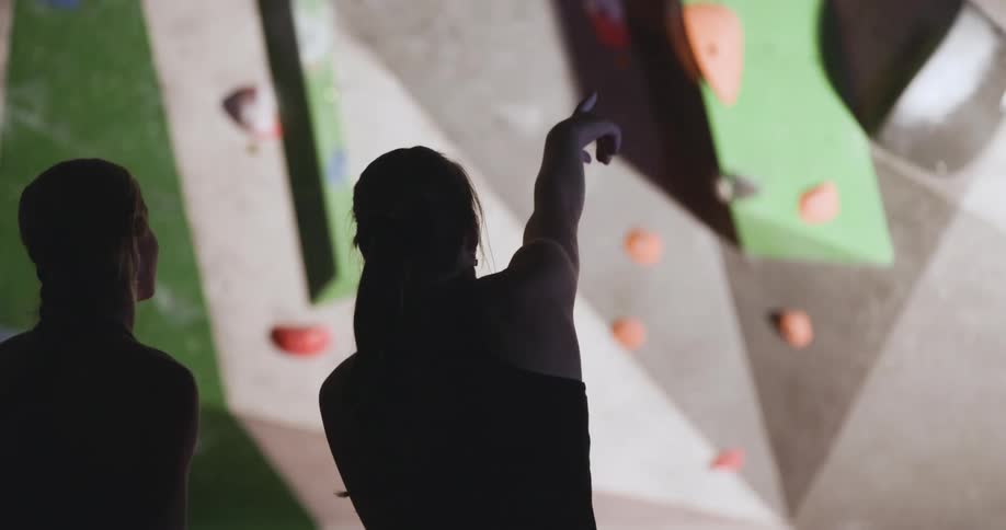 A woman is pointing towards the rock climbing wall