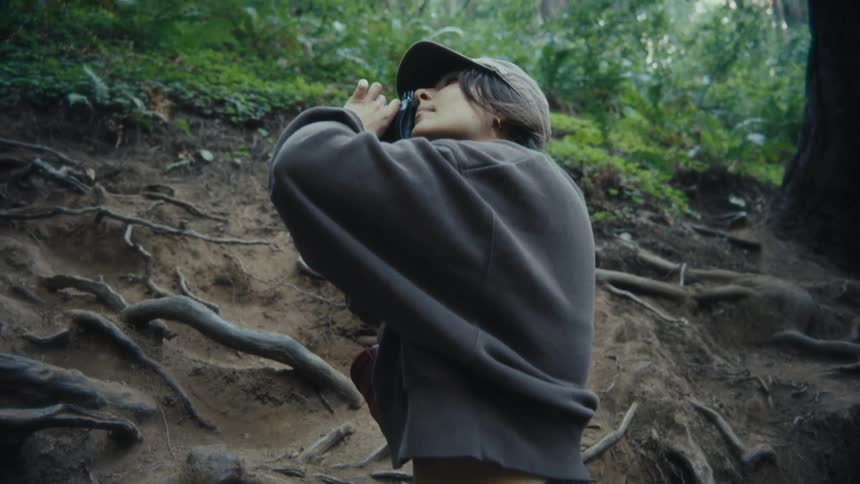 Woman wearing a cap taking a picture while standing in a forest