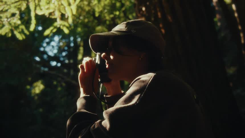 Woman in cap using binoculars in forest