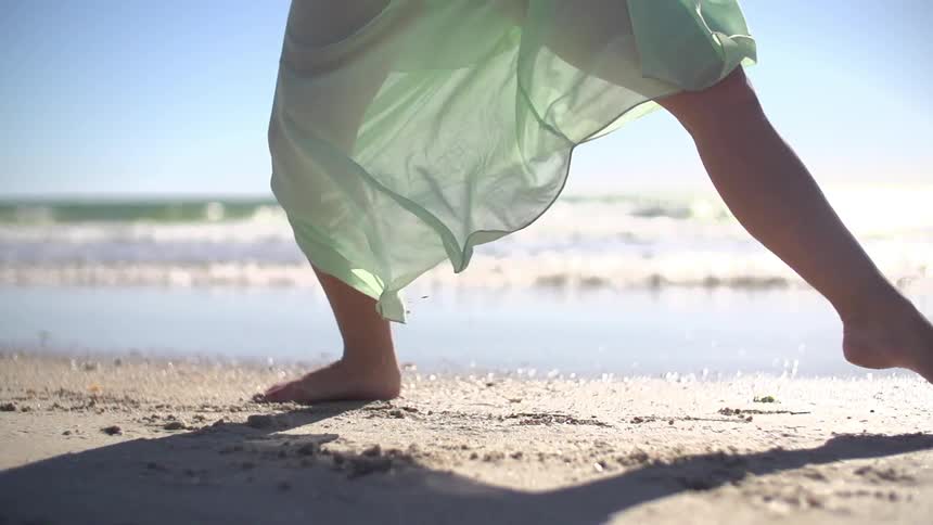 A tight shot of a woman practicing ballet steps on the beach as waves roll to shore behind her