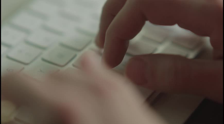 Fingers type closely on a white keyboard