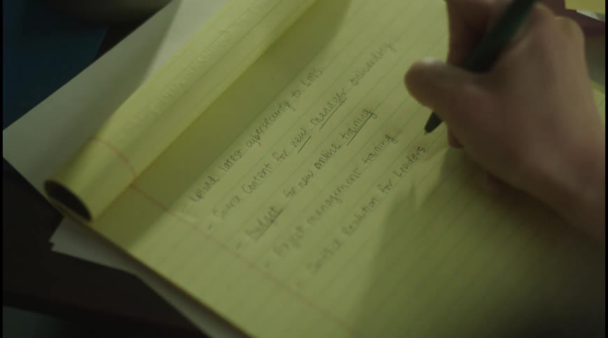 Hand writes on a yellow notepad with a task list