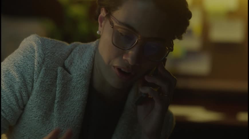 Woman wearing glasses talks on the phone in a workspace with soft lighting