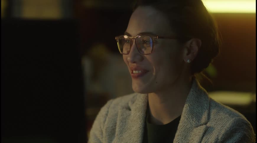 Woman wearing glasses smiles while looking at the computer screen