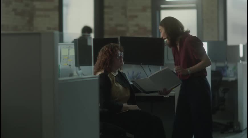 Two coworkers review documents among office cubicles