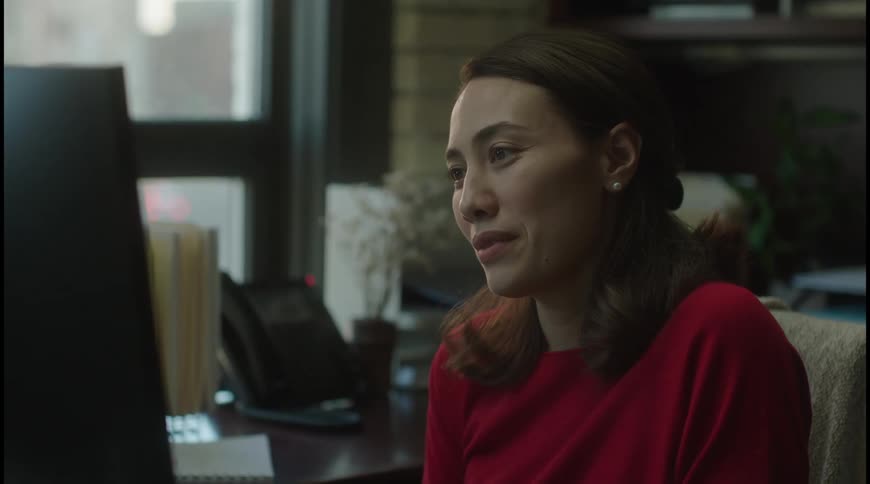 Woman in a red blouse sitting in front of a computer smiling while talking