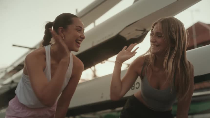 Two smiling women highfive next to rowing boats