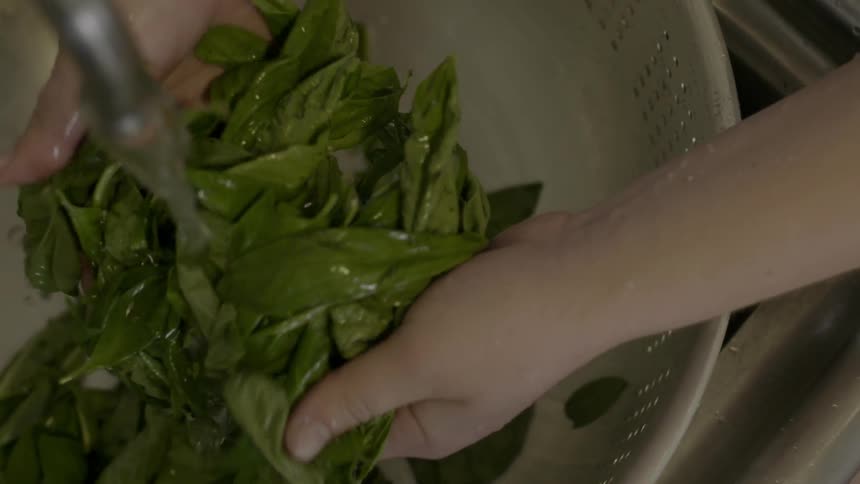 A person washes greens in a colander