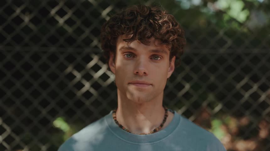 Portrait of a man wearing a necklace and blue t-shirt in front of a fence