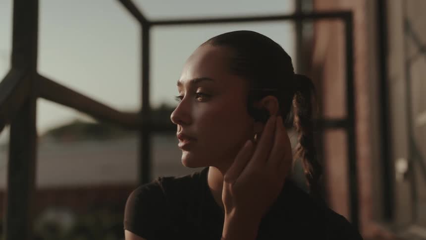 Woman with a braid adjusts her earphone while looking to the side outdoors