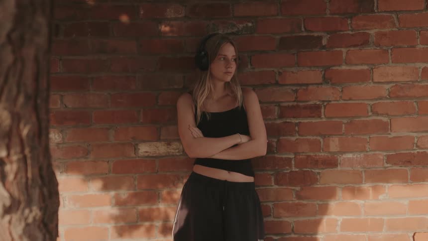 A teenager puts on headphones by a brick wall