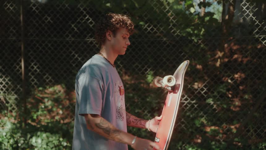 A person walks along a fence and holds a skateboard by his side