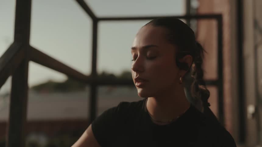 Woman with a braid drinks water from a black bottle while wearing earphones