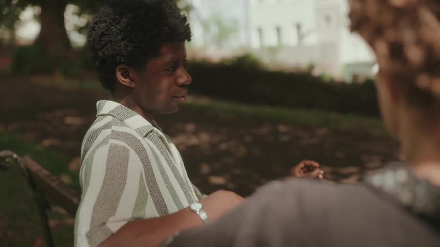 Man in striped shirt gestures while talking seated on a park bench