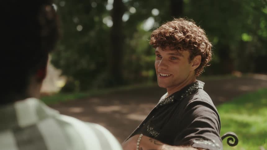Man with curly hair animatedly gestures while talking outdoors