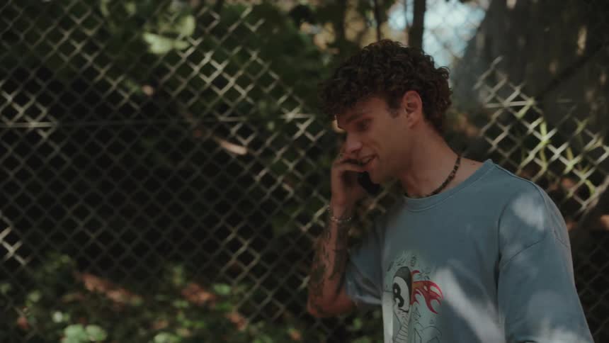 Tattooed man smiles while talking on the phone in front of a fence