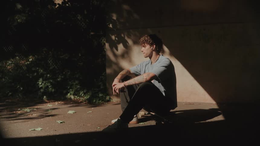 Man with headphones sitting on a skateboard outdoors