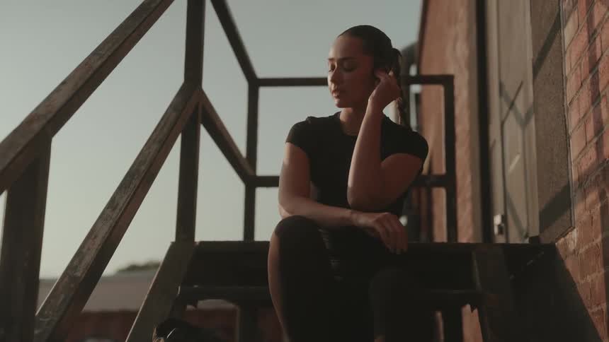 Woman sitting on an outdoor metal staircase adjusts her earphone