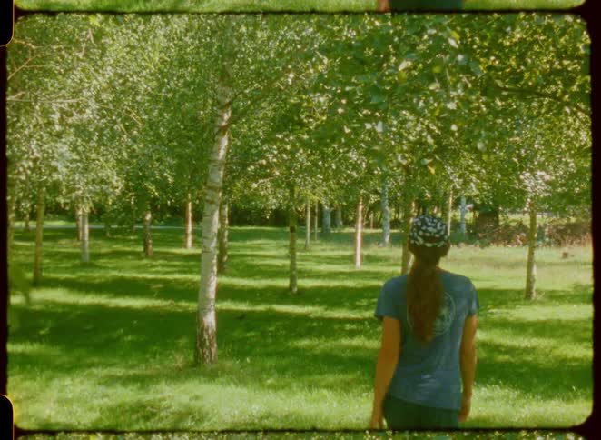 Woman with a cap and braid walks among aligned trees in a green park