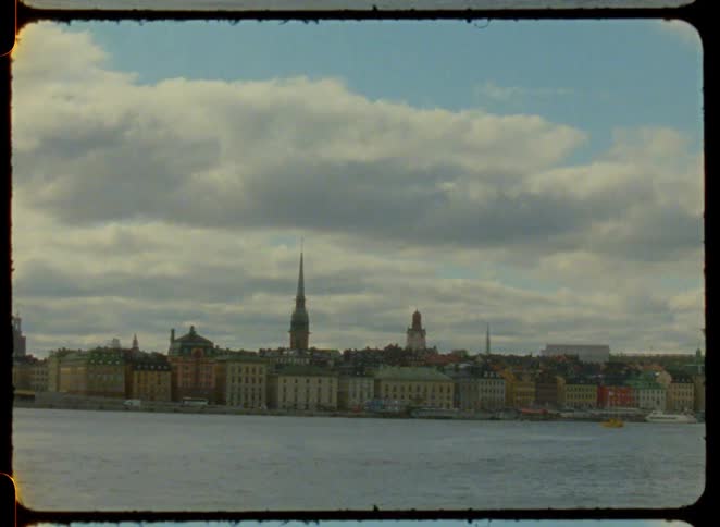The video shows a city with buildings and a bridge on a riverbank under a cloudy sky