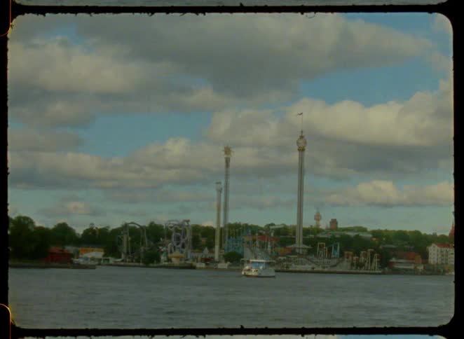 Amusement park by the river with tall towers and roller coasters in the background