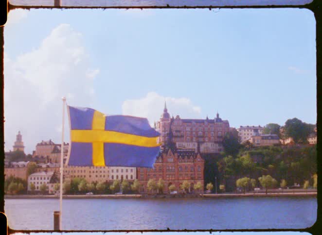 Swedish flag waves by the river with historic buildings in the background