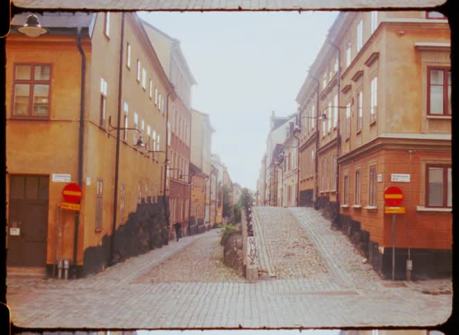 A street with cobblestone and sidewalks on an incline with buildings on either side