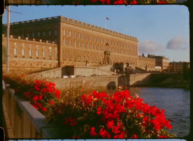 Historic building by a riverside with red flowers prominently in the foreground