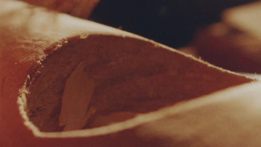 A carpenter blows on a recently carved hoe in a piece of wood clearing the shavings