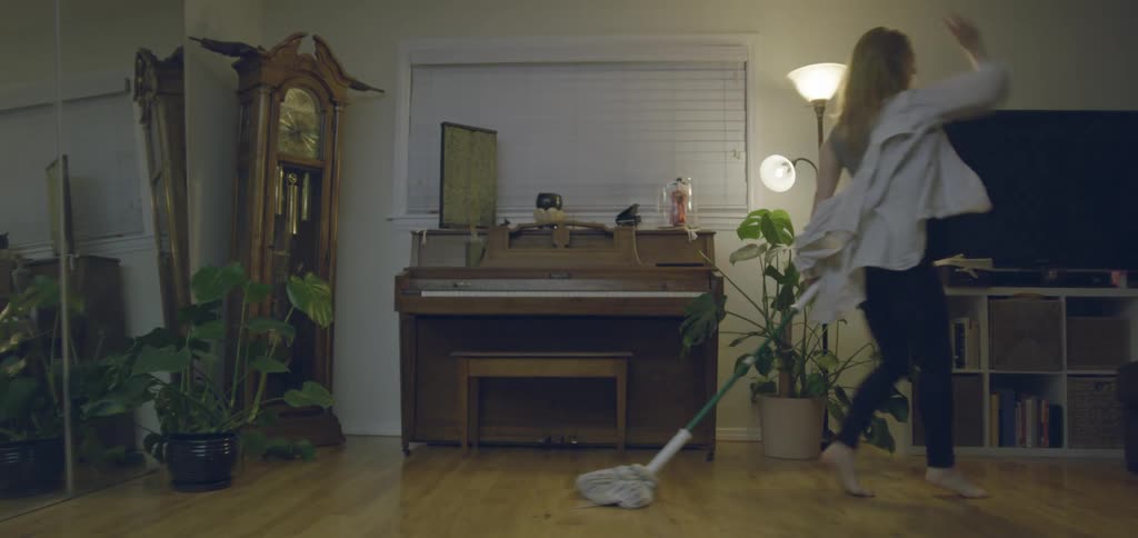 Young woman dancing and laughing while mopping the floor in a living room indoors
