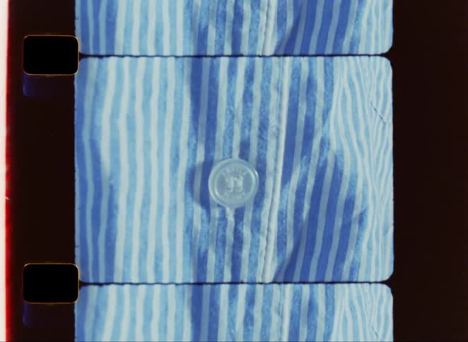A piece of clothing with blue and white stripes and several white buttons is shown in a close view through the rectangular frame of a film strip