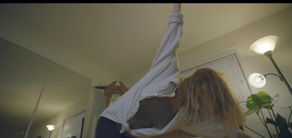 Young woman laughing and dancing while mopping the floor in a living room indoors