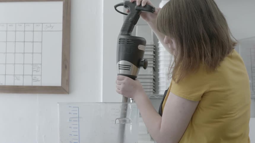 A woman is mixing a large container full of liquid with a machine