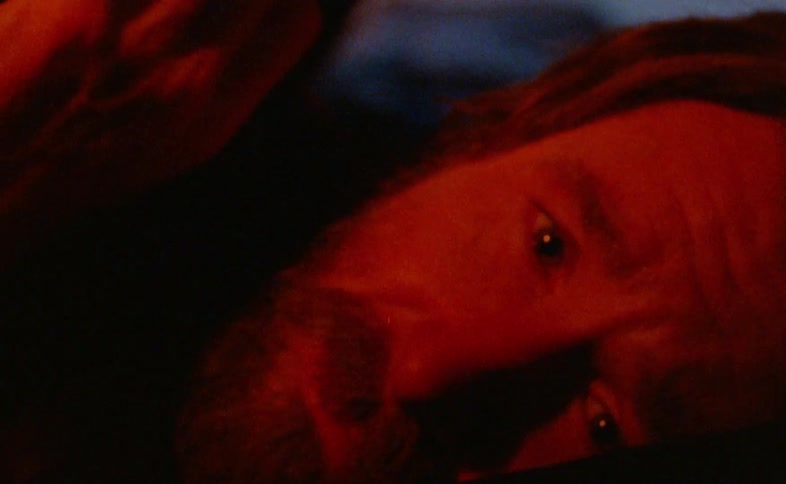 Face of a bearded man lying down scared covering himself with a blanket indoors