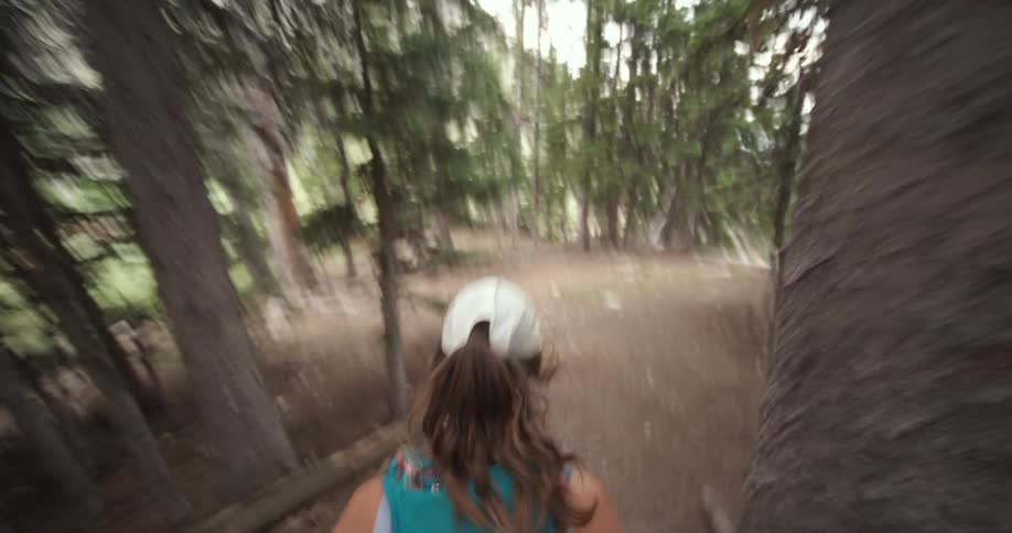 A woman walks on a dirt trail in a forest with trees on both sides of the path
