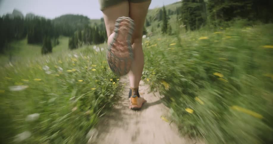 Legs of a white man running outdoors next to a forest and a hill during day time