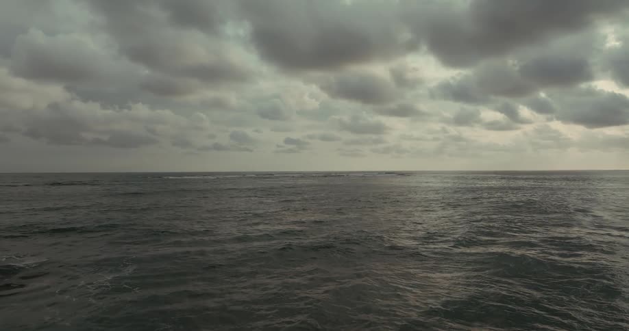 A vast gray ocean stretches to the horizon under a cloudy sky the water is choppy with gentle waves and a thin white line on the horizon indicates a distant shoreline or breakwater