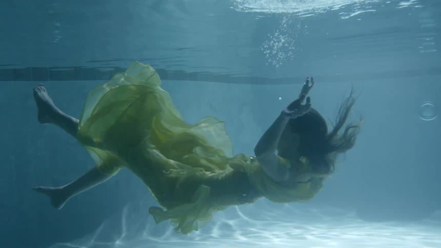 A woman wearing a yellow dress is spinning in the water